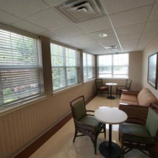 A cozy waiting room with tables and chairs arranged near large windows letting in natural light.