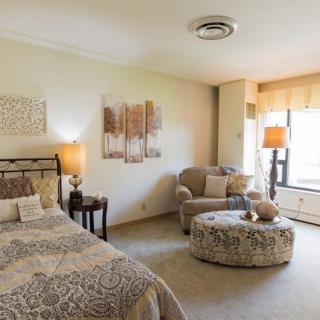 A cozy bedroom with a comfortable bed, armchair, and ottoman, featuring soft lighting and elegant decor.