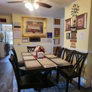 A cozy dining area featuring a large table with chairs, decorated walls with artwork and family photos, under a ceiling fan.