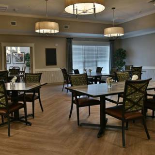 A quiet dining room with neatly arranged tables and chairs, illuminated by stylish overhead lighting.