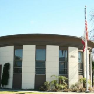 A modern circular building with a flagpole and surrounding plants on a clear day.