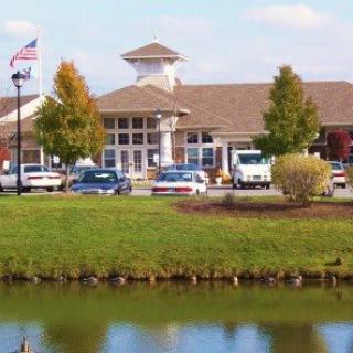 A building with a parking lot in front, surrounded by trees and a pond.