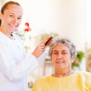 A caregiver gently combing the hair of an elderly woman in a nursing home.