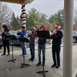 A group of musicians performing holiday tunes outdoors, dressed in Santa hats.