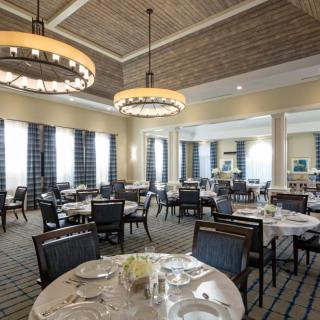 An elegant dining room with neatly arranged tables and chairs, illuminated by chandeliers.