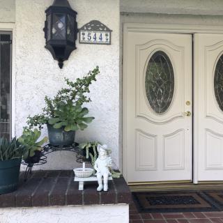 A welcoming front porch with double doors, adorned with plants and a small statue under a traditional lantern.