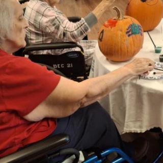 Elderly individuals engaging in pumpkin decorating activities indoors.
