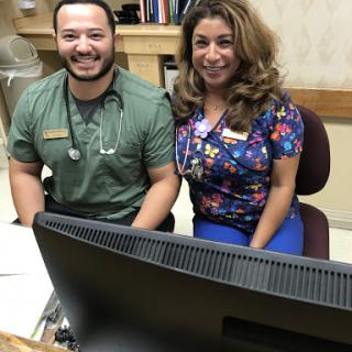Two healthcare staff members smiling together at their desk in an office setting.