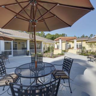 A sunny patio with metal chairs and an umbrella-shaded table in a residential area.
