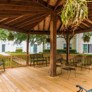 A wooden gazebo with outdoor seating and hanging plants in a garden setting.