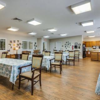 A spacious dining area with multiple tables and chairs, featuring a community kitchen.