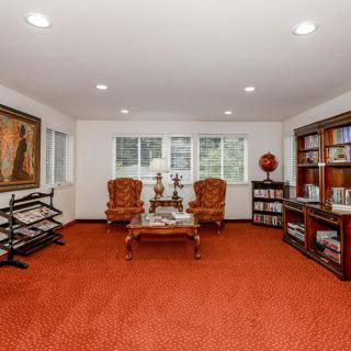 A cozy living room with red carpet, featuring elegant armchairs and well-stocked bookshelves.
