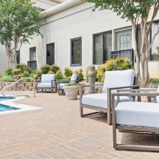 A serene outdoor patio area featuring comfortable seating by a pool, surrounded by lush greenery.