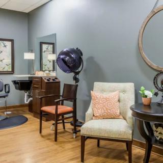 A cozy salon interior with styled chairs, a mirror, and hair drying equipment.