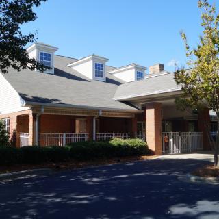 A two-story residential building with a covered entrance surrounded by trees.