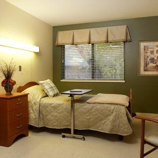 A simple and tidy hospital room with a single bed, bedside table, and window.