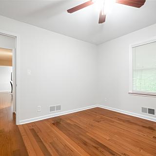An empty room with hardwood floors, white walls, and a ceiling fan.
