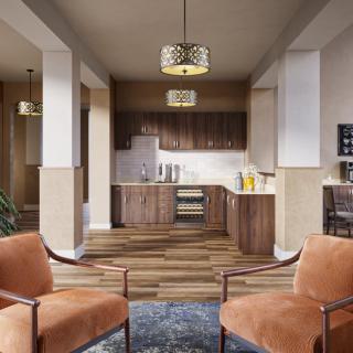 A modern open-plan kitchen and living area featuring wooden cabinets, two orange armchairs, and a stylish chandelier.