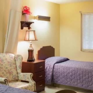 A cozy bedroom with a single bed, nightstand, lamp, and a floral armchair.