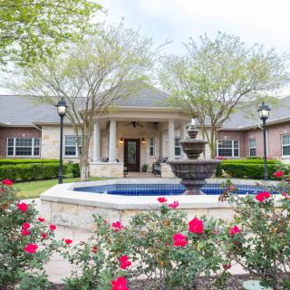 A beautifully landscaped house featuring a central fountain surrounded by vibrant red flowers.