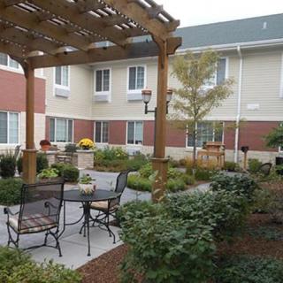A cozy outdoor patio area with a pergola and seating, surrounded by lush landscaping in front of a building.