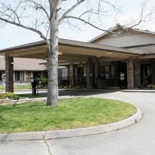 A building with a covered entrance and circular driveway, surrounded by a landscaped area.