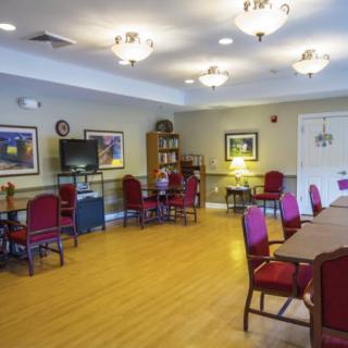A well-lit room with tables and chairs, featuring a television and a bookshelf.