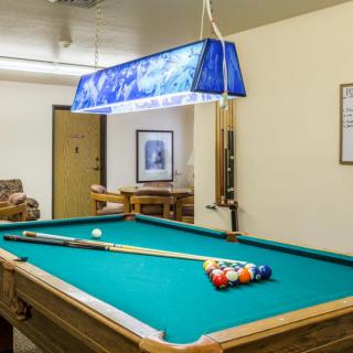 A cozy game room featuring a pool table with a cue stick and billiard balls under bright lighting.
