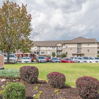 A view of a large building with landscaped greenery and parked cars under a cloudy sky.