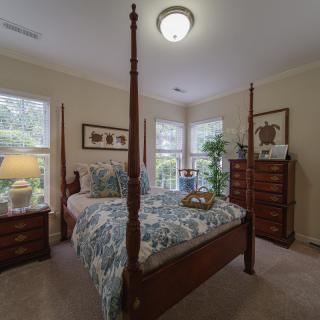 A cozy bedroom with a four-poster bed, surrounded by elegant furniture and bright natural lighting from multiple windows.