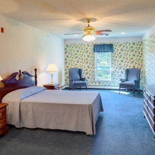 A spacious bedroom with a bed, two chairs, and a window with floral curtains.