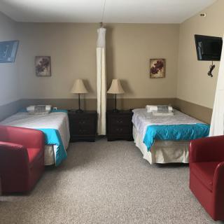 A hotel room with twin beds, featuring cozy seating and wall-mounted televisions.