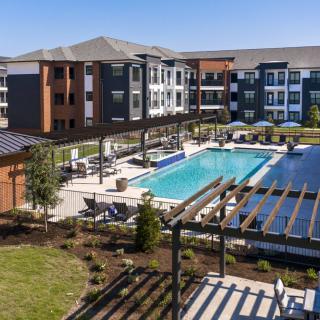 A modern apartment complex featuring a large swimming pool and landscaped outdoor area.