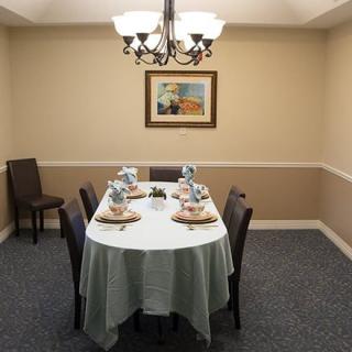 A neatly set dining table with a chandelier overhead and artwork on the wall.