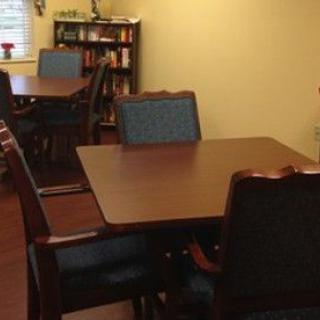 A dining room with wooden tables and chairs, and a bookshelf in the corner.