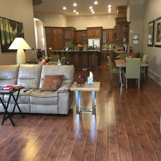 A spacious living room with an open floor plan leading to a kitchen and dining area, featuring wood flooring and comfortable seating.