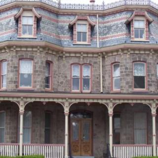 A historic Victorian stone house with an ornate porch and multiple windows.