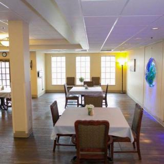 A cozy dining area with neatly arranged tables and chairs, featuring a wooden floor and large windows that allow natural light to brighten the space.