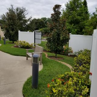 A landscaped garden pathway with a white fence, surrounded by lush greenery and plants.