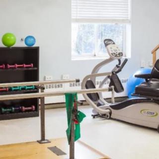 A rehabilitation room equipped with an elliptical machine, therapy bars, light weights, and exercise balls.