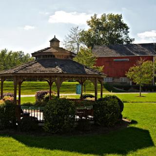 A picturesque view of a gazebo surrounded by lush greenery and a charming building in the background.