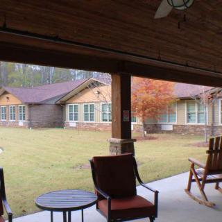 A cozy patio with rocking chairs and a table overlooking a well-maintained lawn and building.