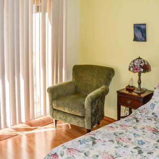 A cozy bedroom corner with a green armchair, floral bedspread, and a stained glass lamp on a wooden side table.