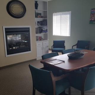 A cozy meeting room with a conference table and chairs, featuring a fireplace and bookshelf.