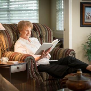 An elderly woman comfortably reading a book in her cozy living room.