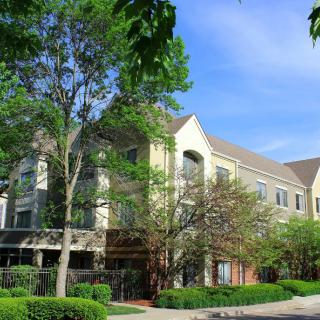 A residential apartment building surrounded by lush greenery and trees on a sunny day.