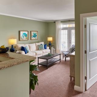 A cozy living room with green walls, featuring a comfortable sofa, stylish artwork, and elegant lighting.