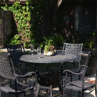 A sunny patio with a round metal table and chairs, surrounded by greenery.