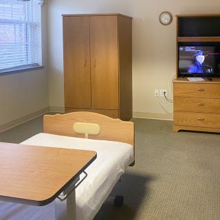A simple hospital room with a bed, wardrobe, and television.