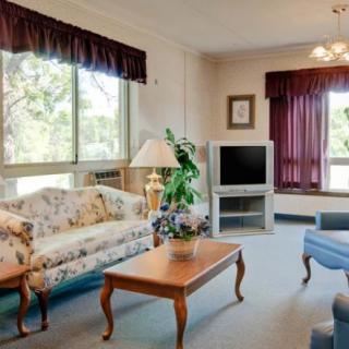 A cozy living room with a floral sofa, coffee table, and television set beside large windows.